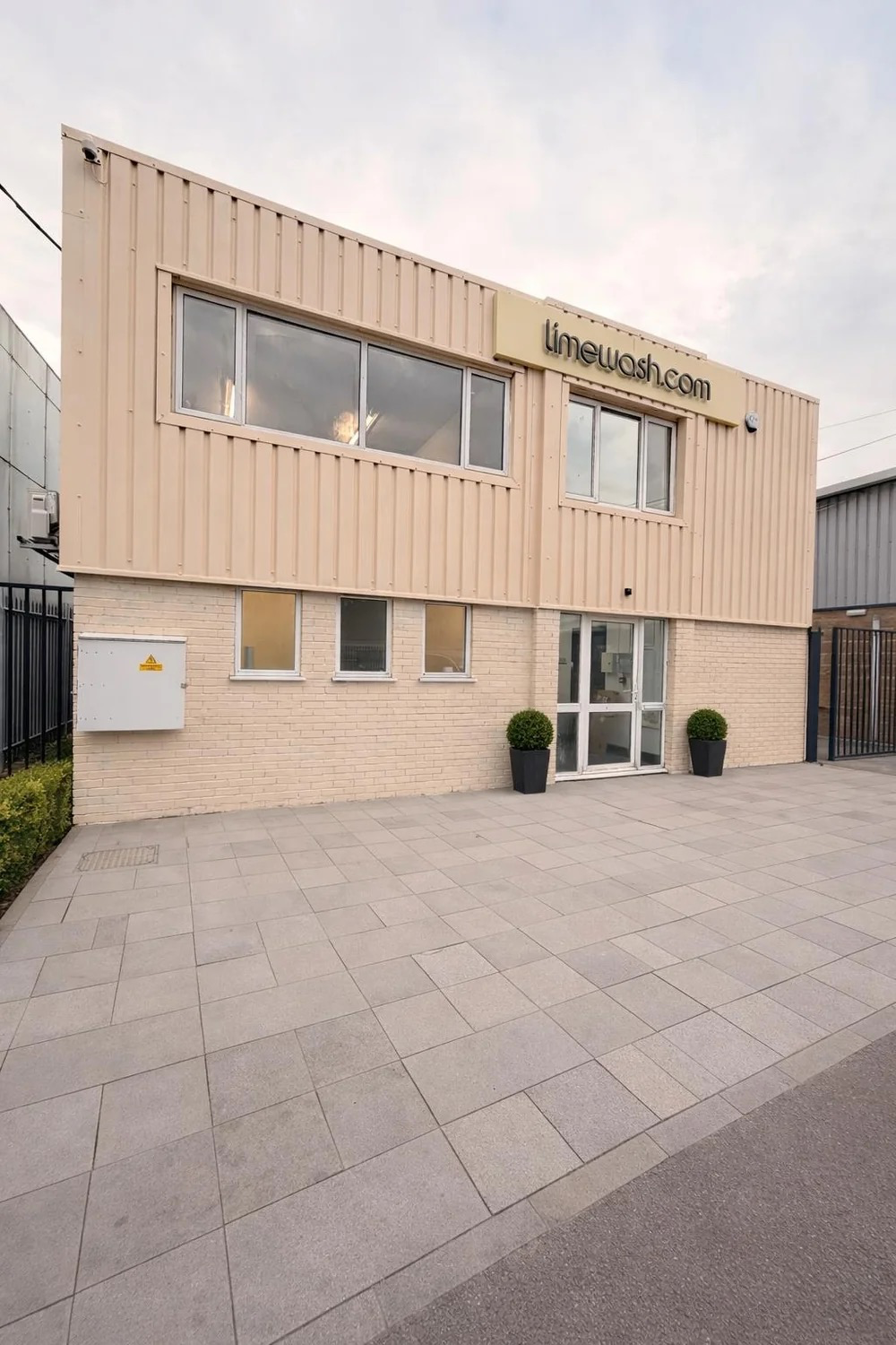 Limewash.com production building in Marden, Kent — cream corrugated-clad walls over a brick lower level, the limewash.com sign and grey paved forecourt